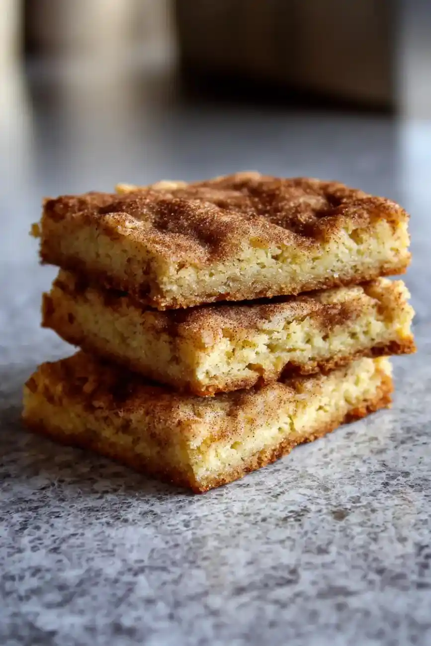 Stack of chewy cinnamon snickerdoodle cookie bars on a marble surface.