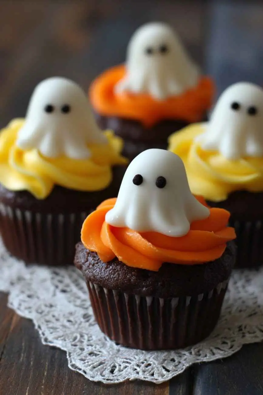 Chocolate Halloween cupcakes topped with fondant ghost decorations and orange and yellow buttercream swirls.