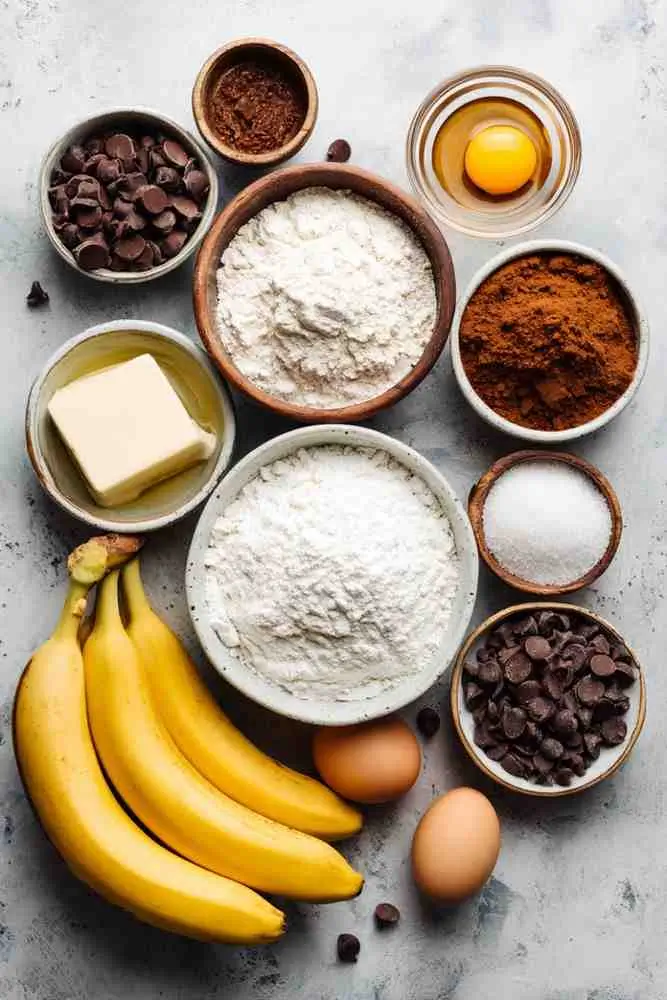 Baking ingredients for pumpkin chocolate chip muffins, including bananas, flour, eggs, butter, sugar, and chocolate chips.