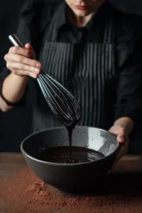 Whisking melted chocolate ganache in a dark bowl.