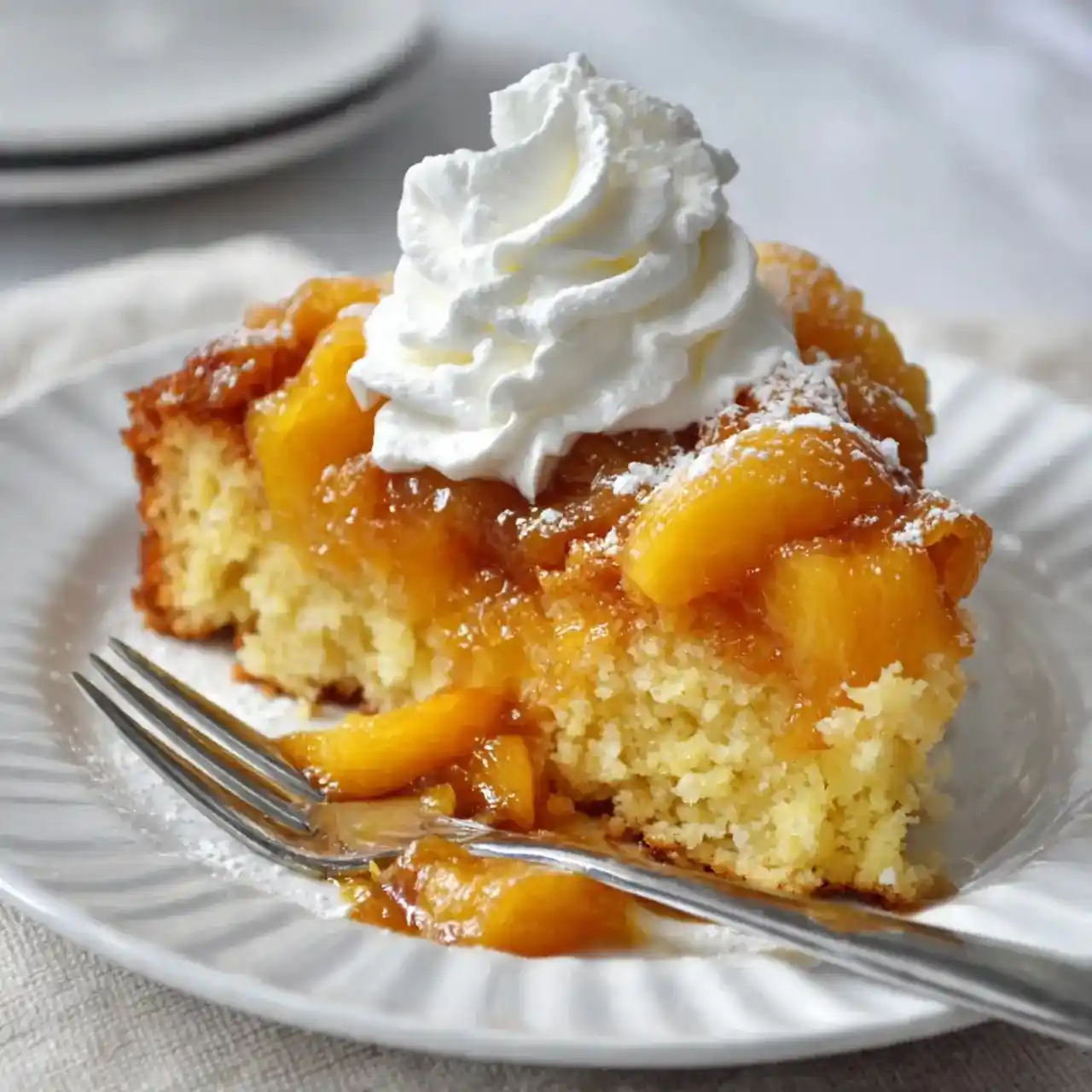 Slice of peach dessert cake topped with whipped cream on a white plate with a fork.
