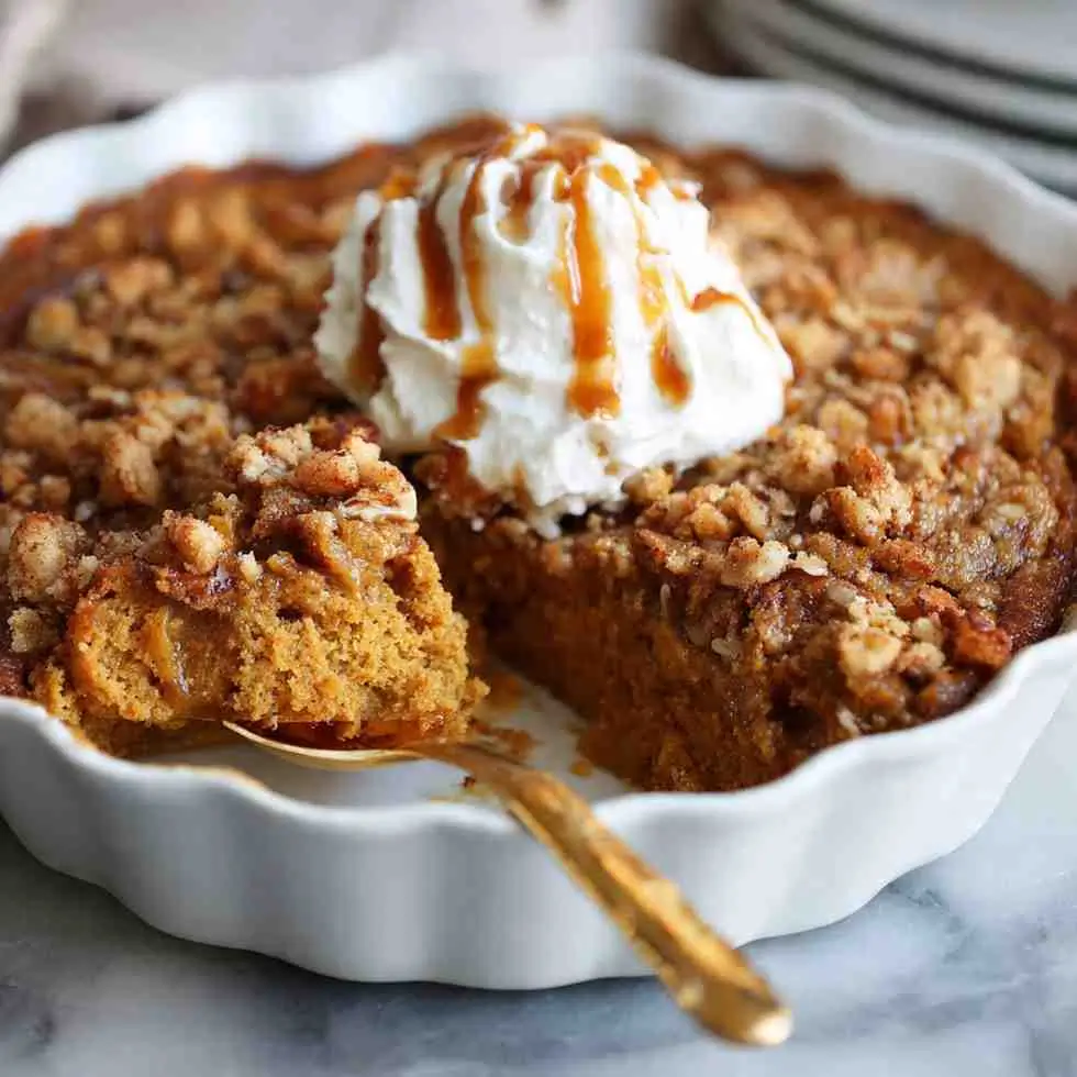 Freshly baked pumpkin dump cake in a round dish topped with whipped cream and caramel drizzle.
