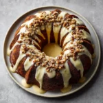 Finished glazed eggnog bundt cake topped with chopped nuts and thick icing on a round plate.